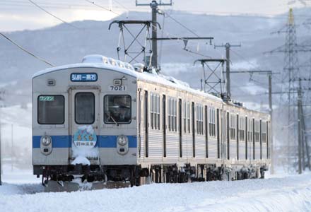 積もった雪の中、館田駅に接近する弘南鉄道7000系４両編成